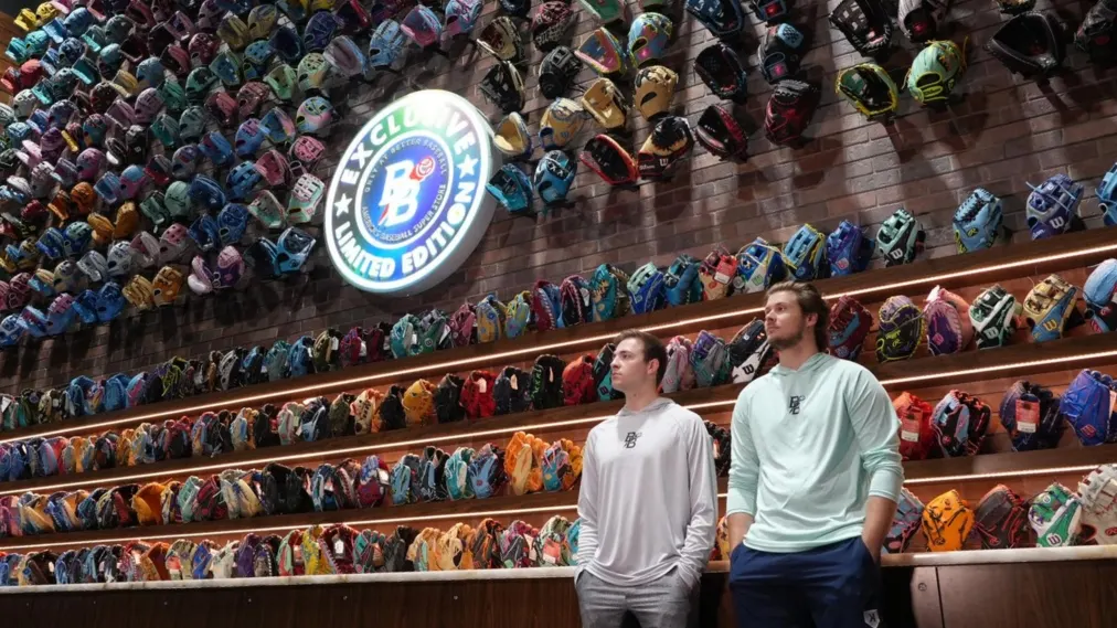 Two Better Baseball staff in front of the store's wall of exclusive gloves